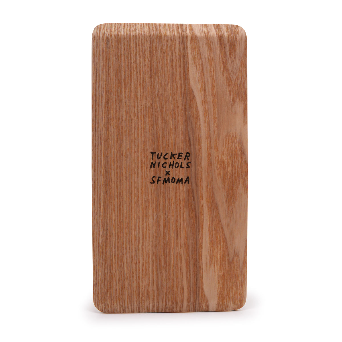 A rectangular wooden board with rounded corners, featuring a natural light brown wood grain texture and the black printed text 'TUCKER NICHOLS x SFMOMA' in the center, set against a plain white background.