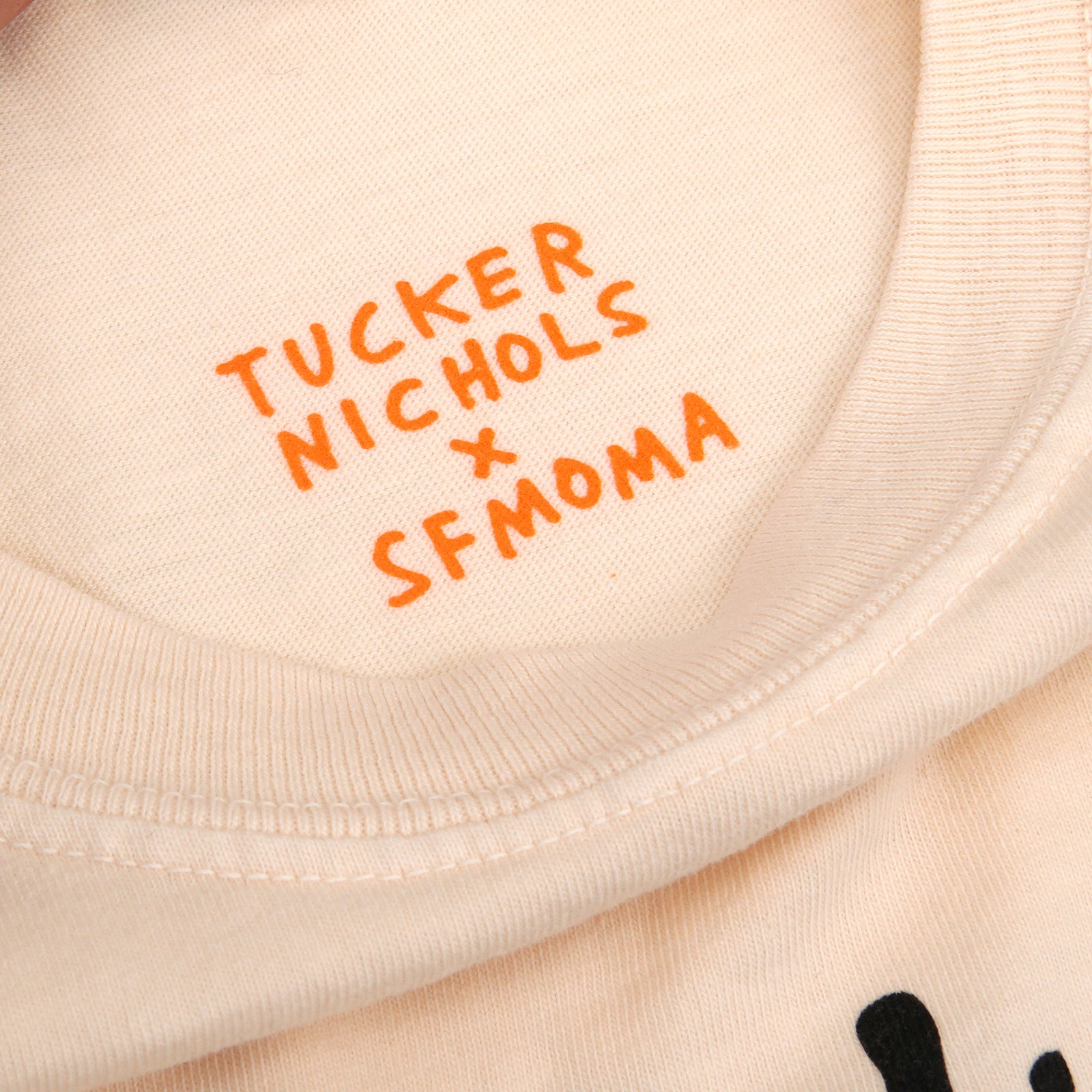 A light beige crewneck t-shirt featuring a black line art graphic of a hand holding a bouquet of flowers on the front, displayed flat against a white background.