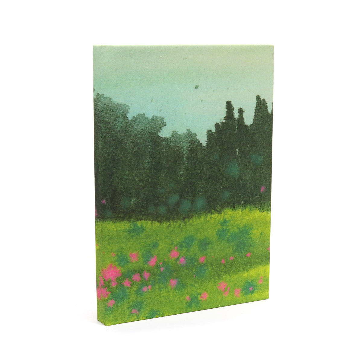 A front cover notebook featuring a landscape painting of a green field with pink flowers and a dark tree line under a pale sky, shown on a white background.