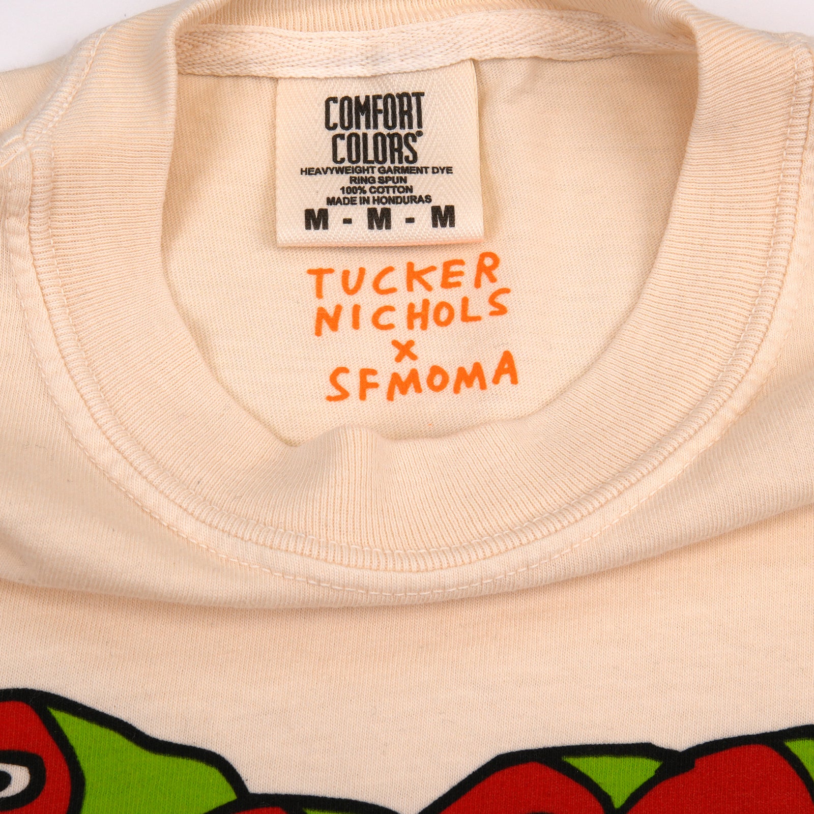 A light cream-colored short-sleeve t-shirt with a graphic of three cartoon birds in red and orange on a green shape above the text 'SAN FRANCISCO'.