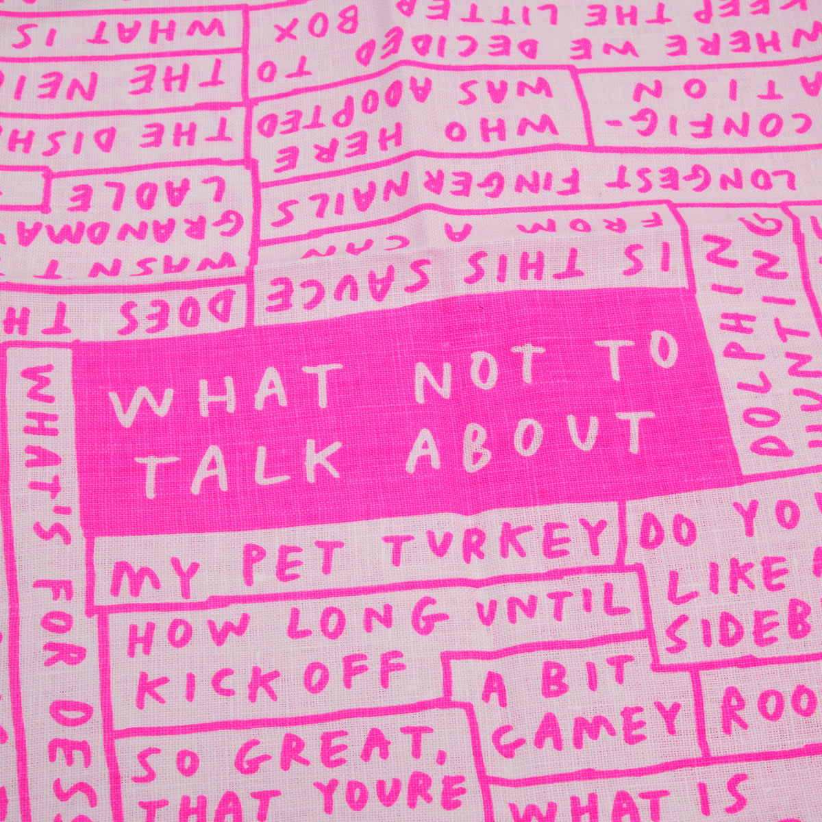 A close-up of a pink and white fabric featuring hand-drawn style text blocks with humorous and awkward phrases like 'WHAT NOT TO TALK ABOUT' and 'MY PET TURKEY'.