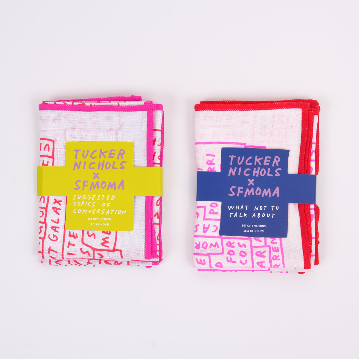 Two folded fabric items with paper bands on a white background. The left item is white with bright pink handwritten-style text and a yellow band reading 'Tucker Nichols x SFMOMA'.