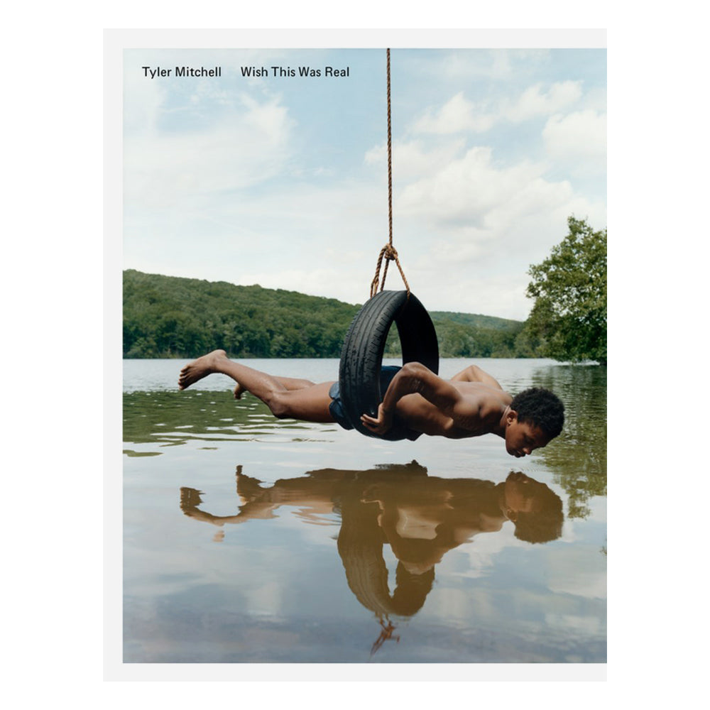 Person lying on a tire swing over water with mountains in the background