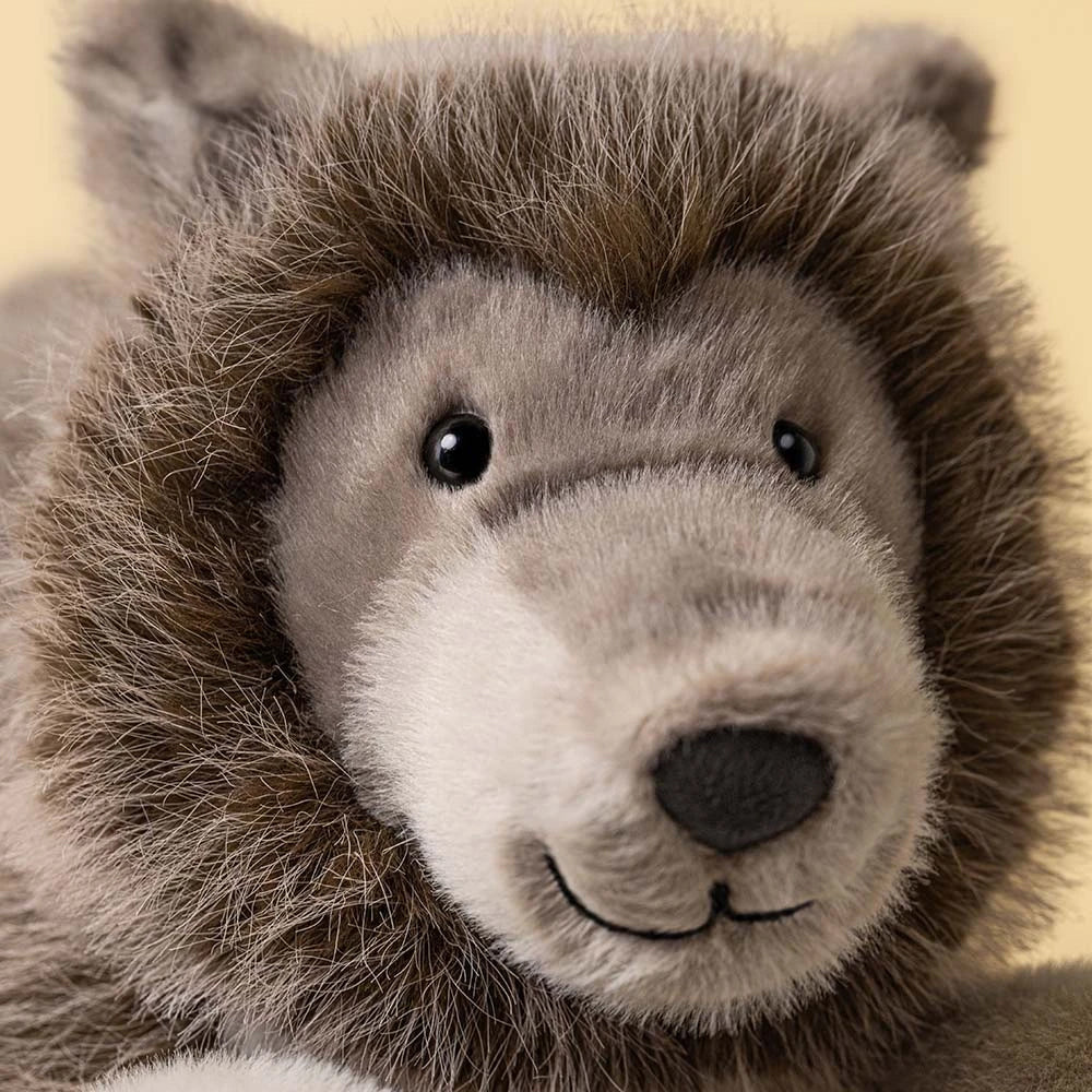 Close-up of a plush stuffed animal head with brown and gray fur, black eyes, and a stitched smile on a pale yellow background.
