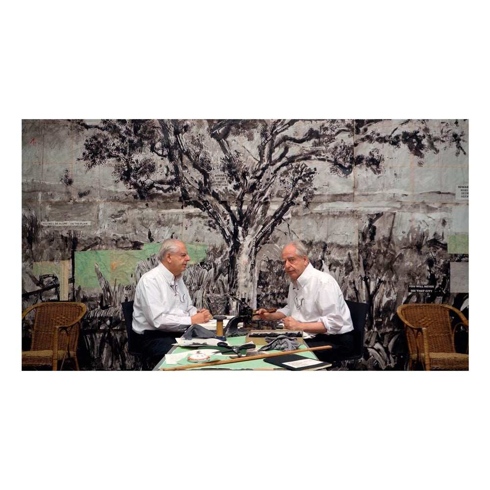 Two men sitting at a table with a large abstract painting in the background
