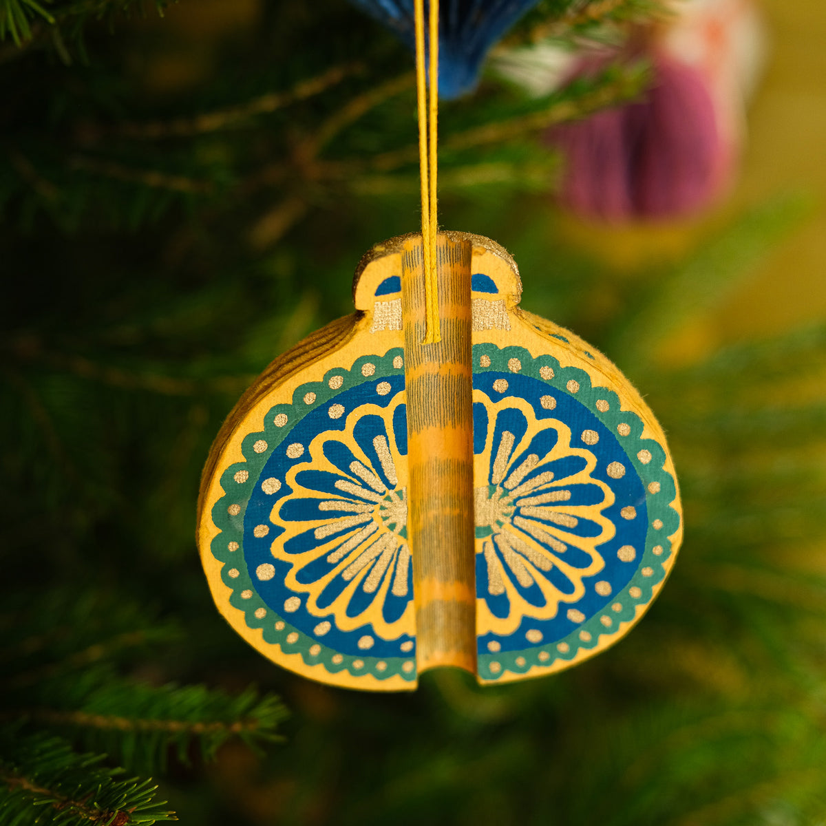 Decorative ornament with blue and yellow design hanging on a tree.