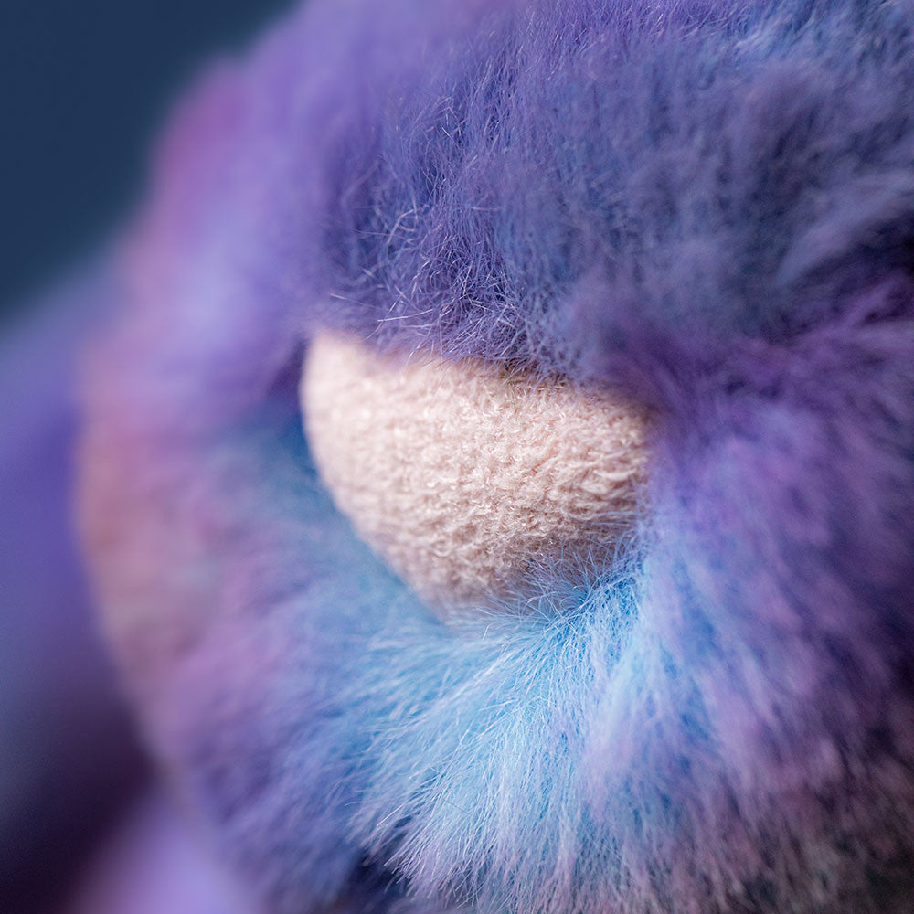 Close-up of pink nose with fluffy purple and blue textured surface.