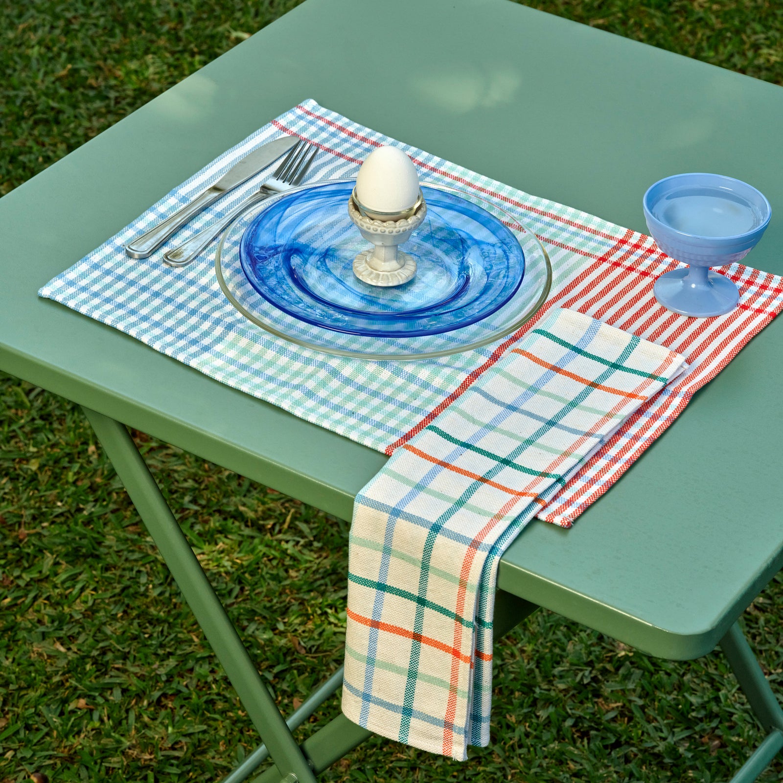 Two square white napkins with a colorful plaid pattern, displayed side-by-side on a plain white background.