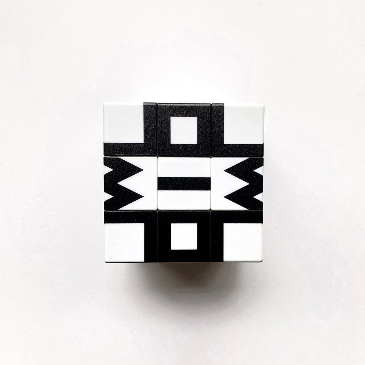 A 3x3 cube-shaped puzzle with a black and white geometric pattern, photographed from directly above on a light gray background.