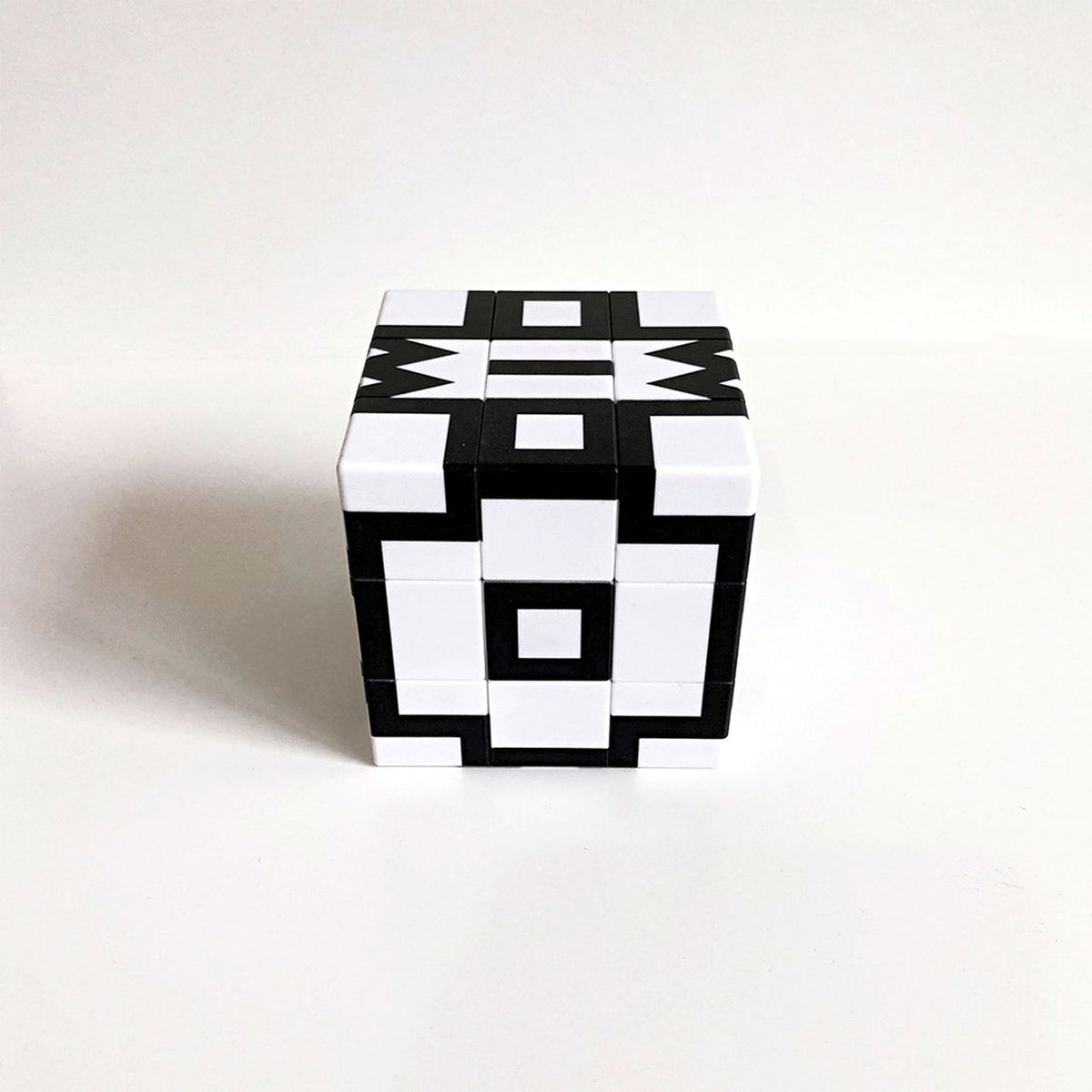 A small cube-shaped geometric puzzle toy with a black and white block pattern, photographed on a plain light background.