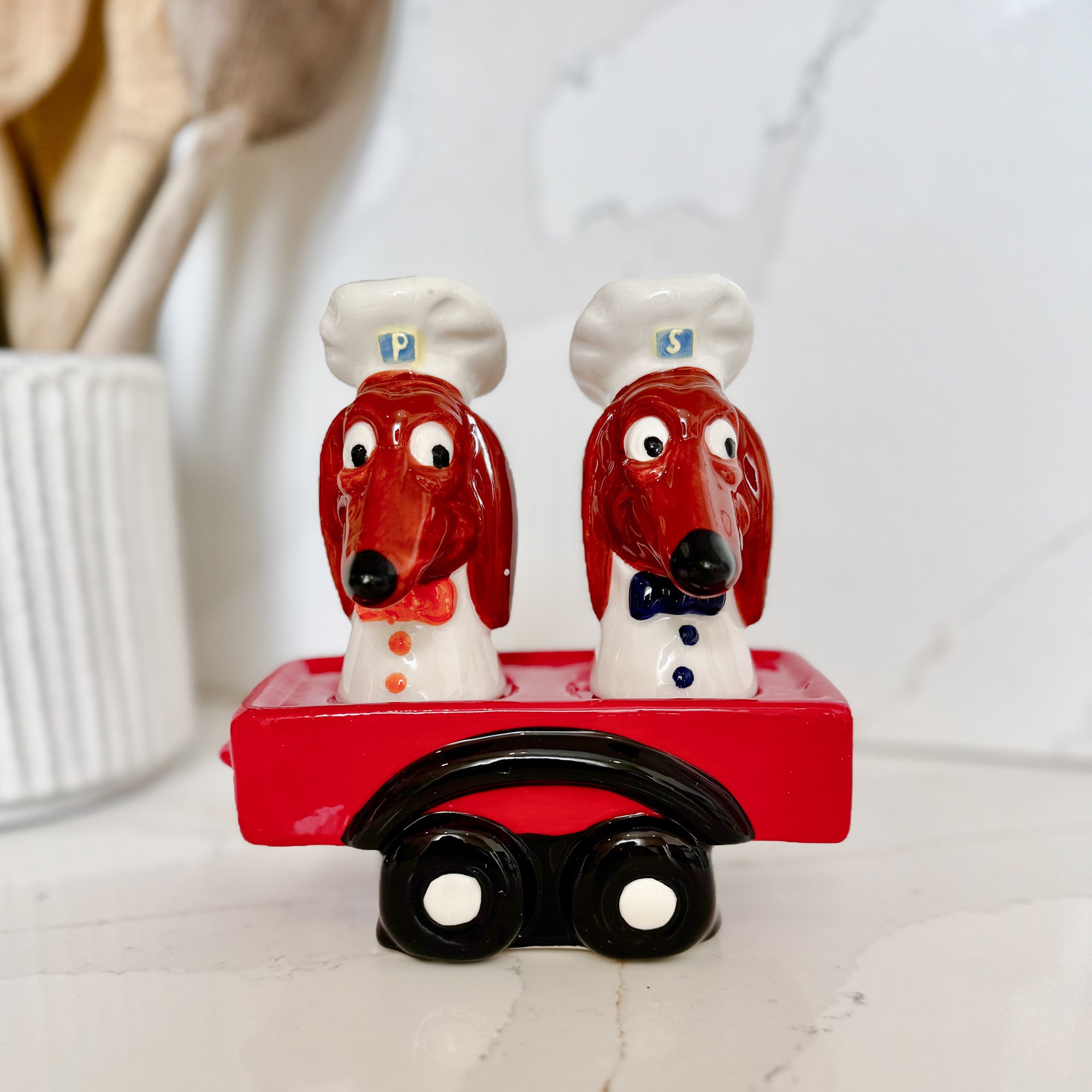 Two dog-shaped salt and pepper shakers with a red cart on a white background
