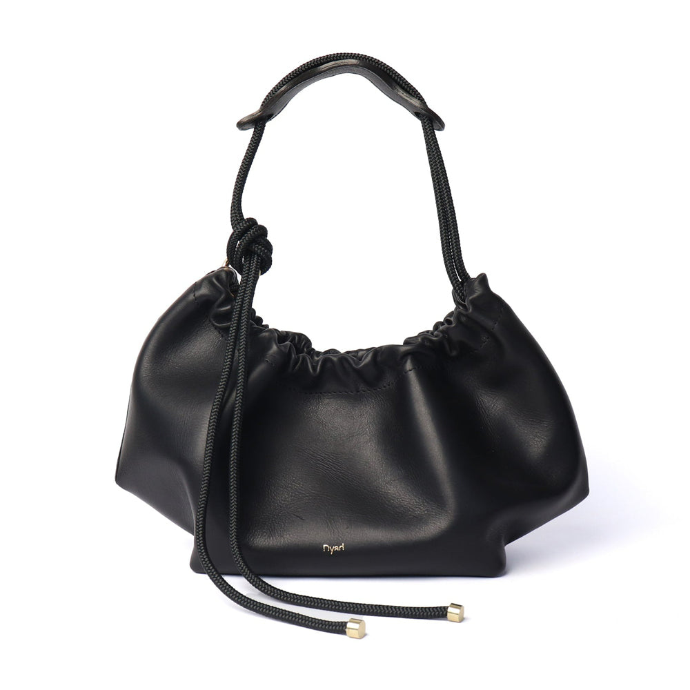 Black leather shoulder bag with ruched detail, asymmetrical knotted strap, and a magnetic fastening. It features an extra long strap and comes with a detachable zip pouch.