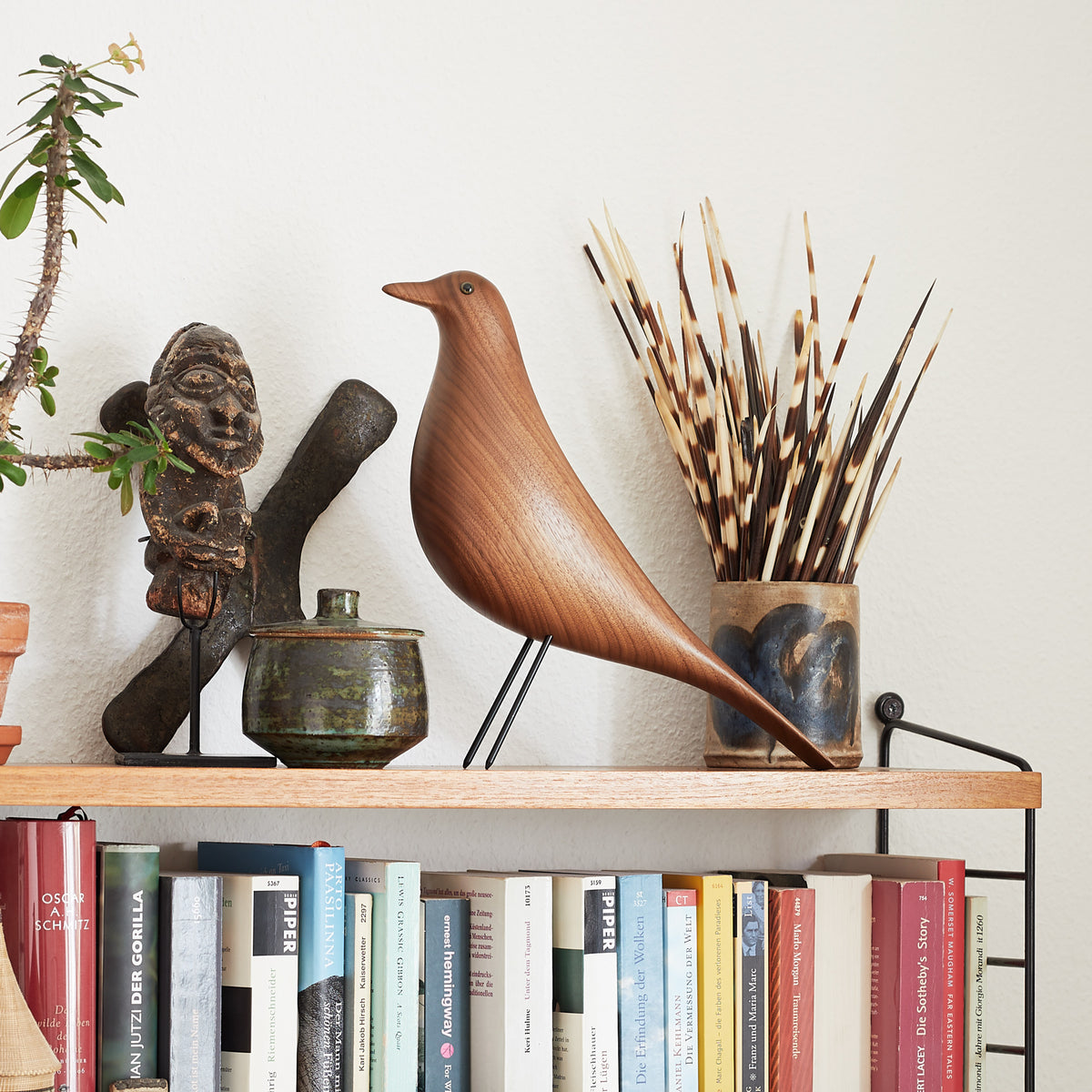 Wooden bird sculpture on a bookshelf with books and decorative items.