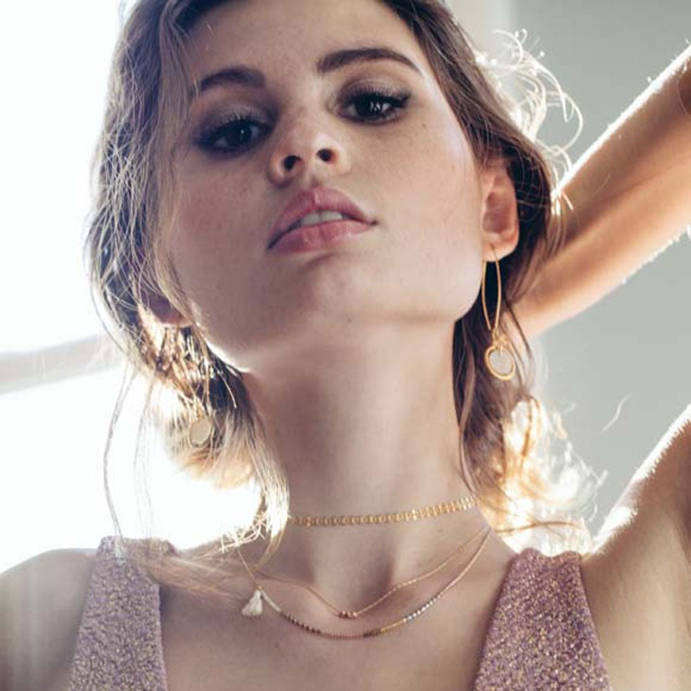Model wearing necklace with other layered necklaces.