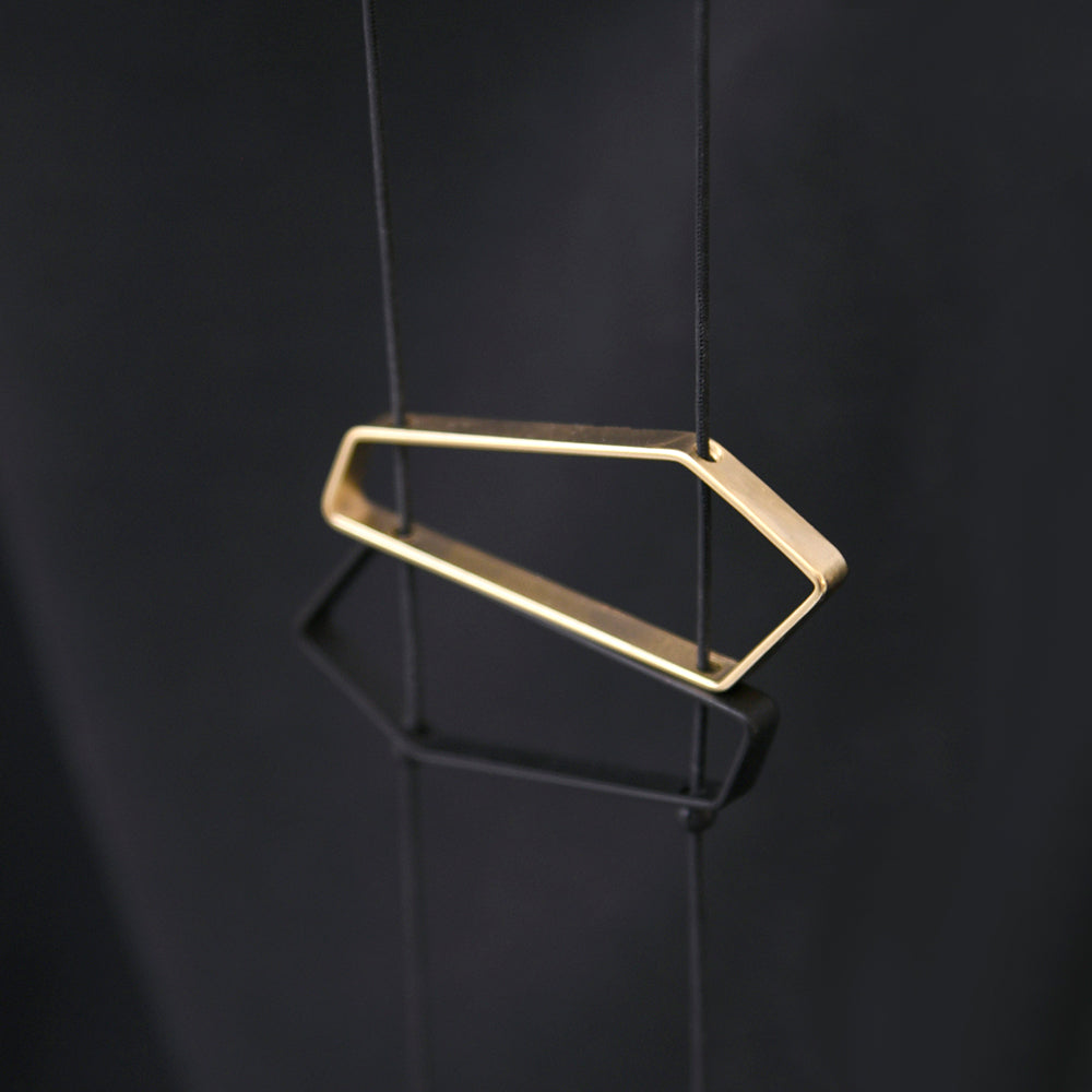 Close up of necklace chain and satin black and gold geometric pendants on black fabric
