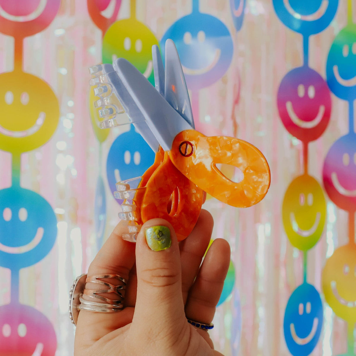 Hand holding a hair claw against a colorful smiley face background