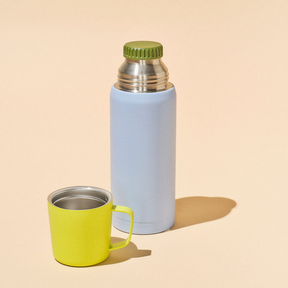 Light blue thermos with green cap and mug on beige background