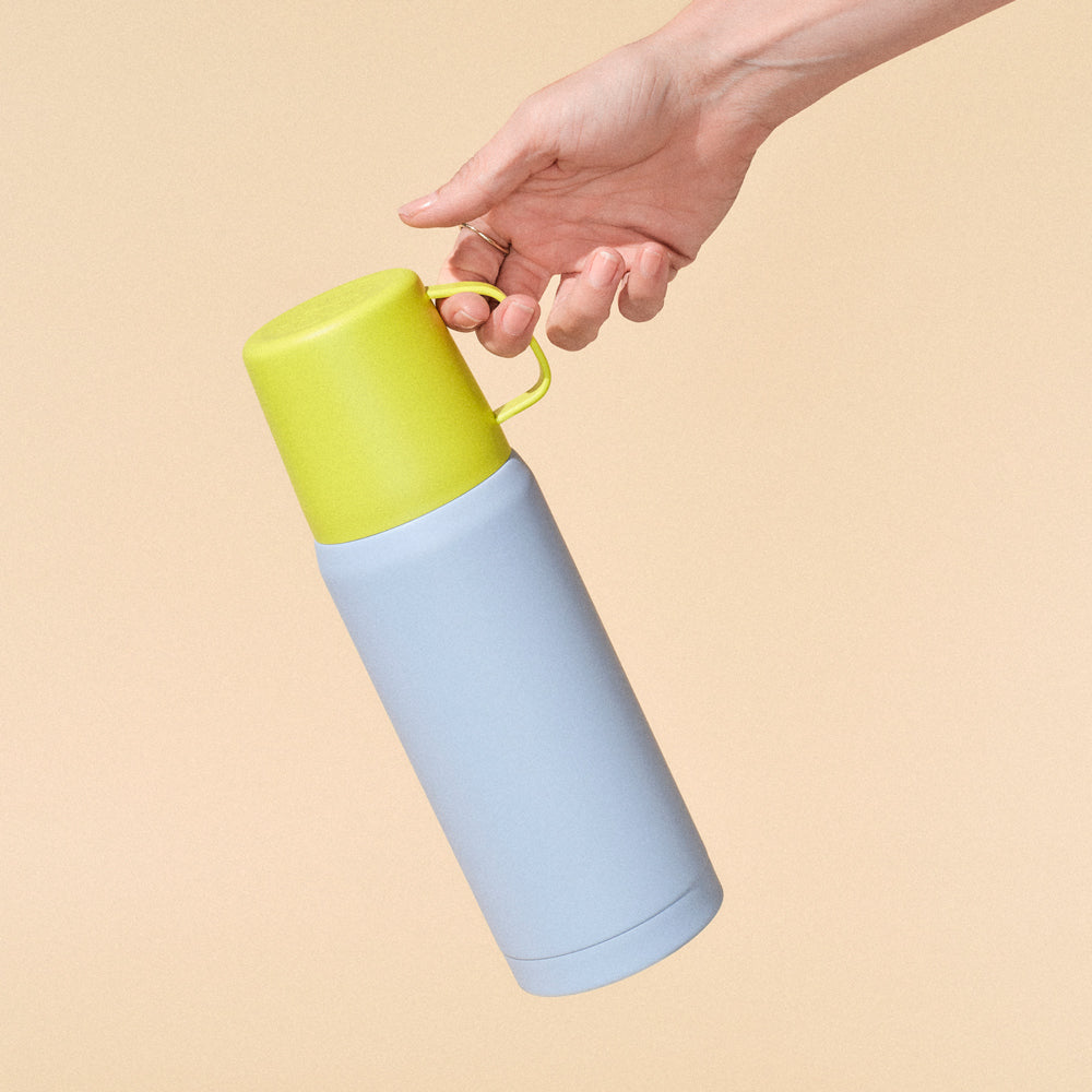 Hand holding a two-toned blue and yellow thermos against a beige background