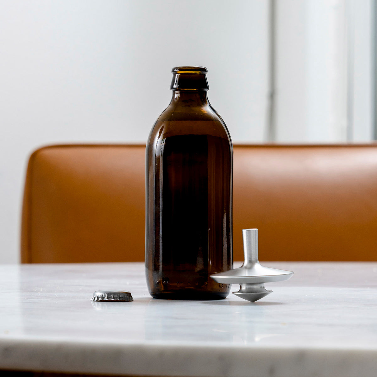 Brown glass bottle with a metal cap on a marble surface with a brown chair in the background.