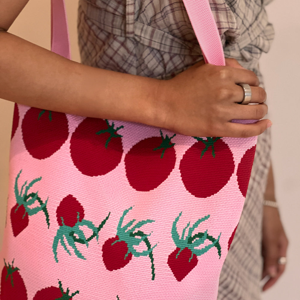 Person holding a pink bag with red tomato pattern