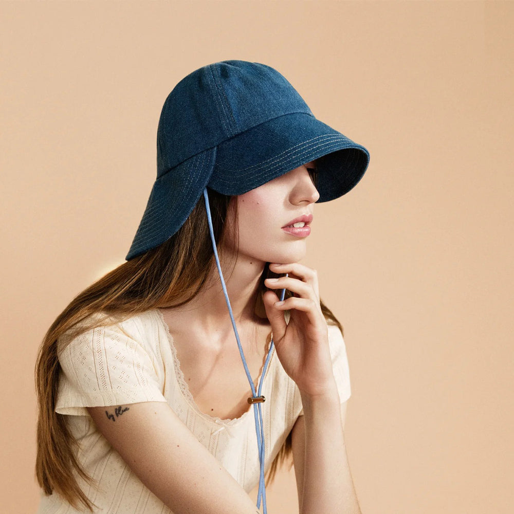 Woman wearing a blue bucket hat against a beige background