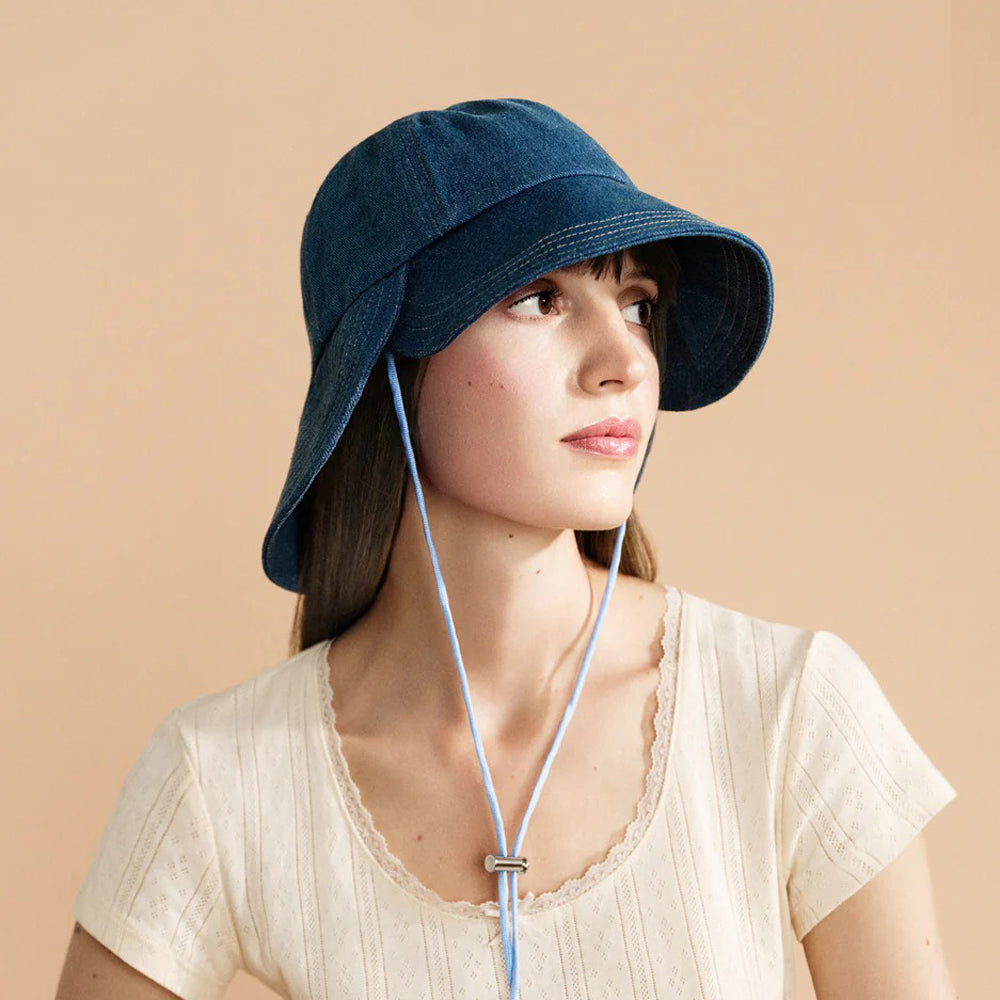Woman wearing a blue denim sun hat on a beige background