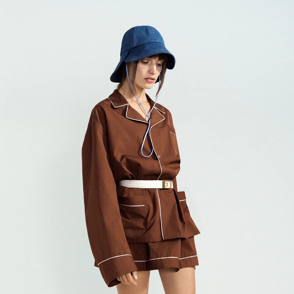 Person wearing a brown outfit with a blue hat on a light gray background