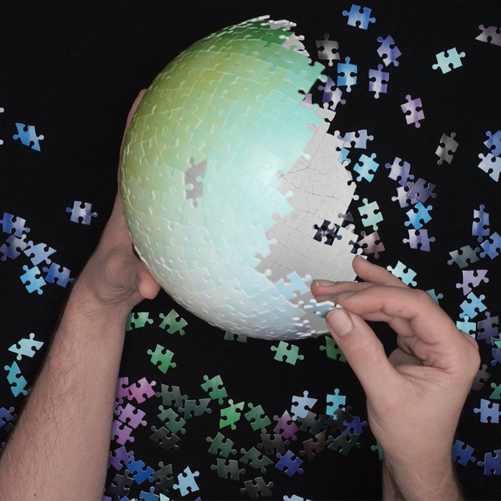 Hands building a 540 Colors Sphere 3-D Jigsaw Puzzle.