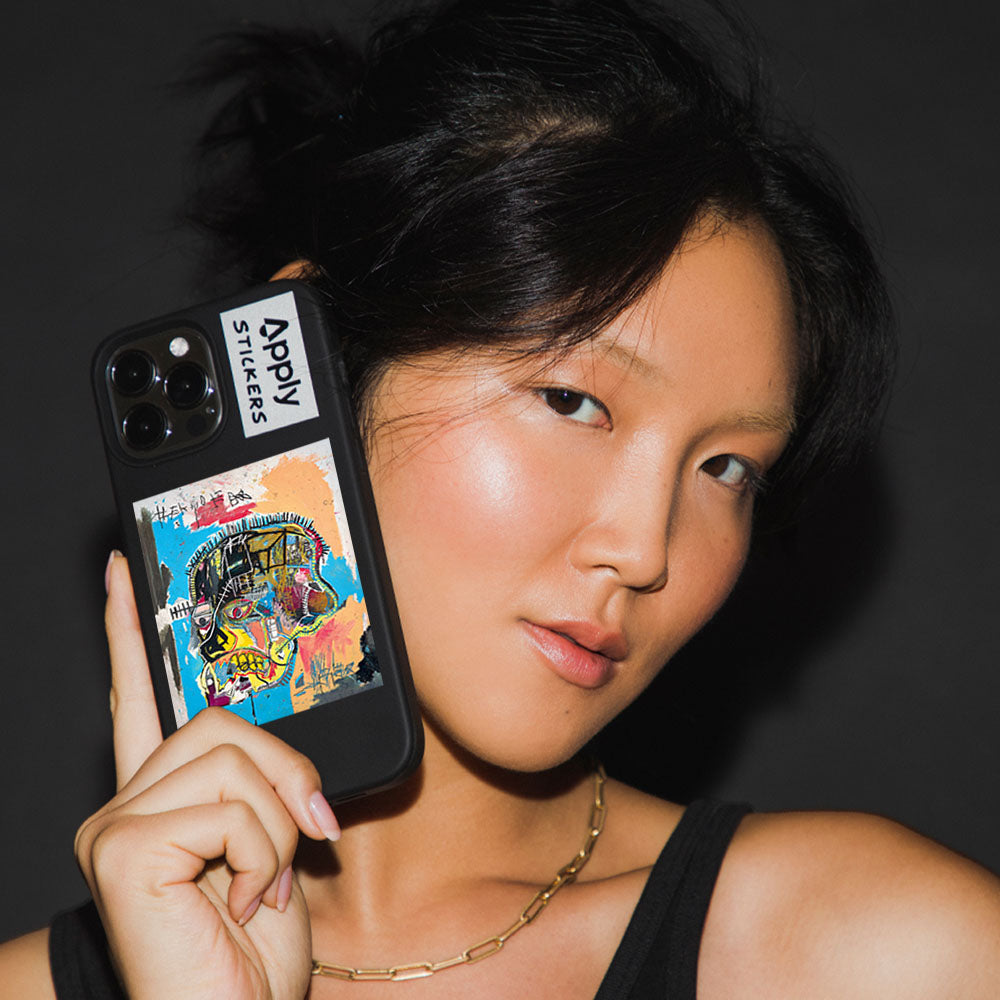 Model holding phone with Basquiat Skull Sticker by Apply Stickers.