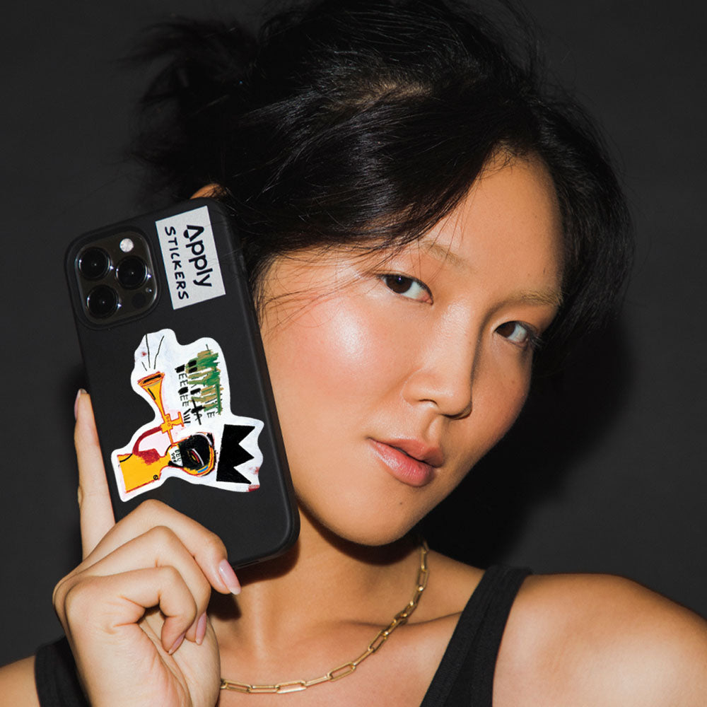 Model holding phone with Basquiat Trumpet Sticker by Apply Stickers.