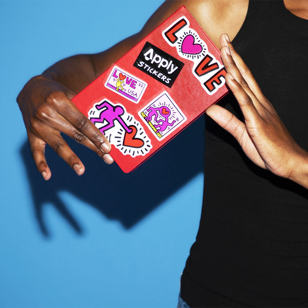 Model holds up red journal, with four Keith Haring &#39;Love&#39; stickers and one Apply sticker.