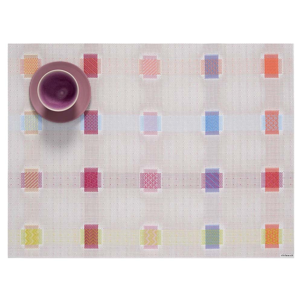 Placemat with a faint plaid pattern with different color combinations at each intersection. Purple teacup top left.