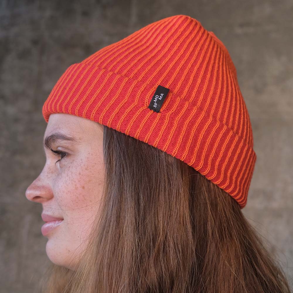 Model Wearing SFMOMA Rib Hat: Red + Poppy in front of concrete background.