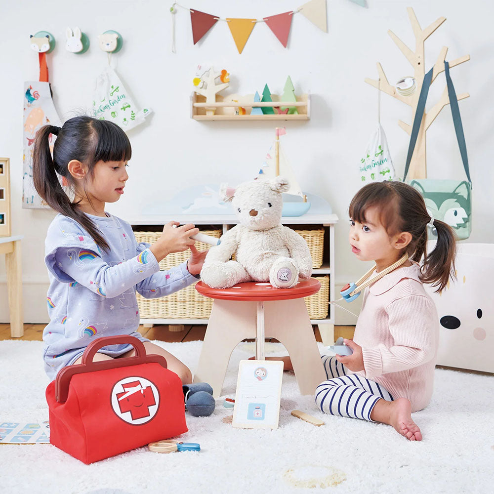 Two kids playing doctor with stuffed bear sitting on Toadstool.