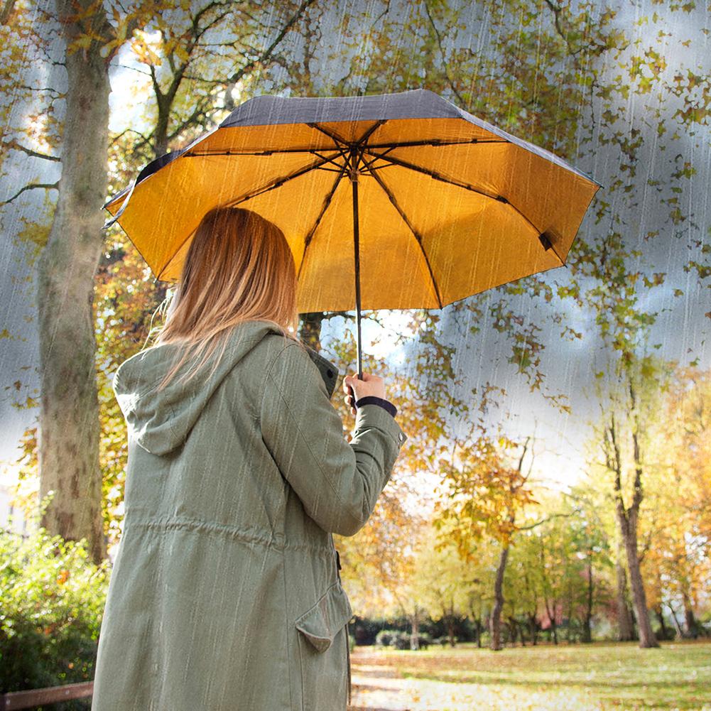 A model using a SFMOMA Black and Gold Umbrella in the rain in a park.
