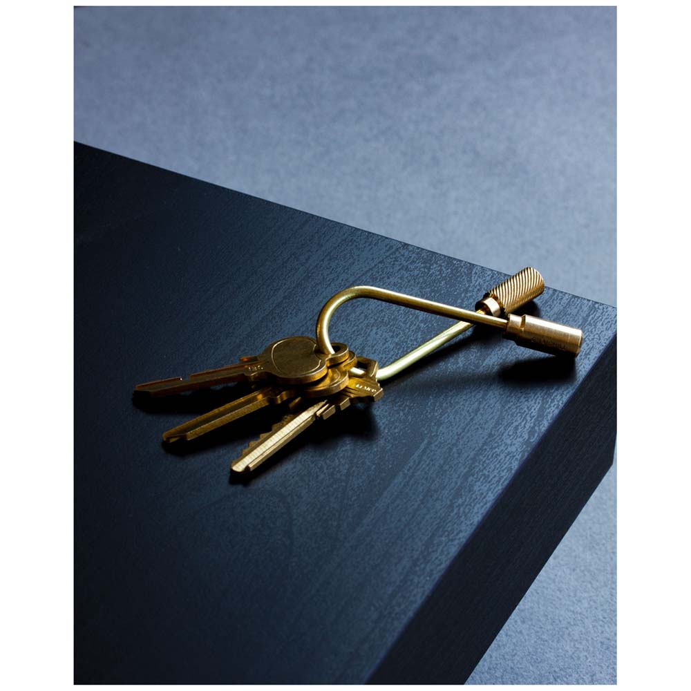 A Closed Helix Keyring: Brass holding three keys on the corner of a black desk.
