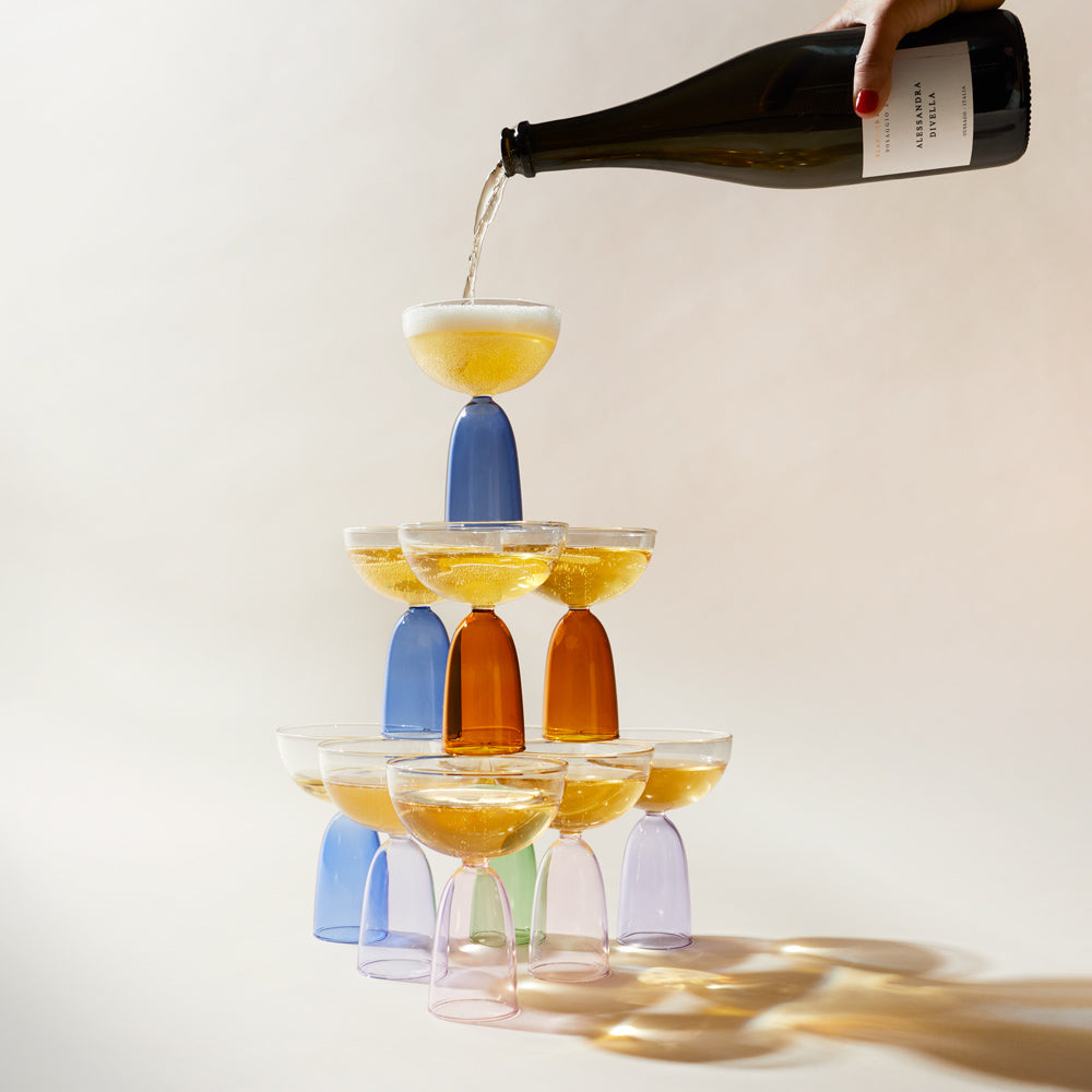 Hand pouring champagne on stacked coupe glasses.