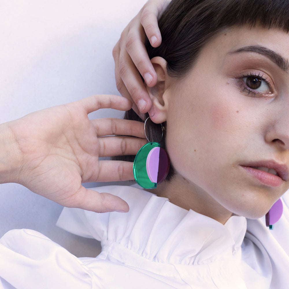 Close-up model wearing earrings with hands close by.