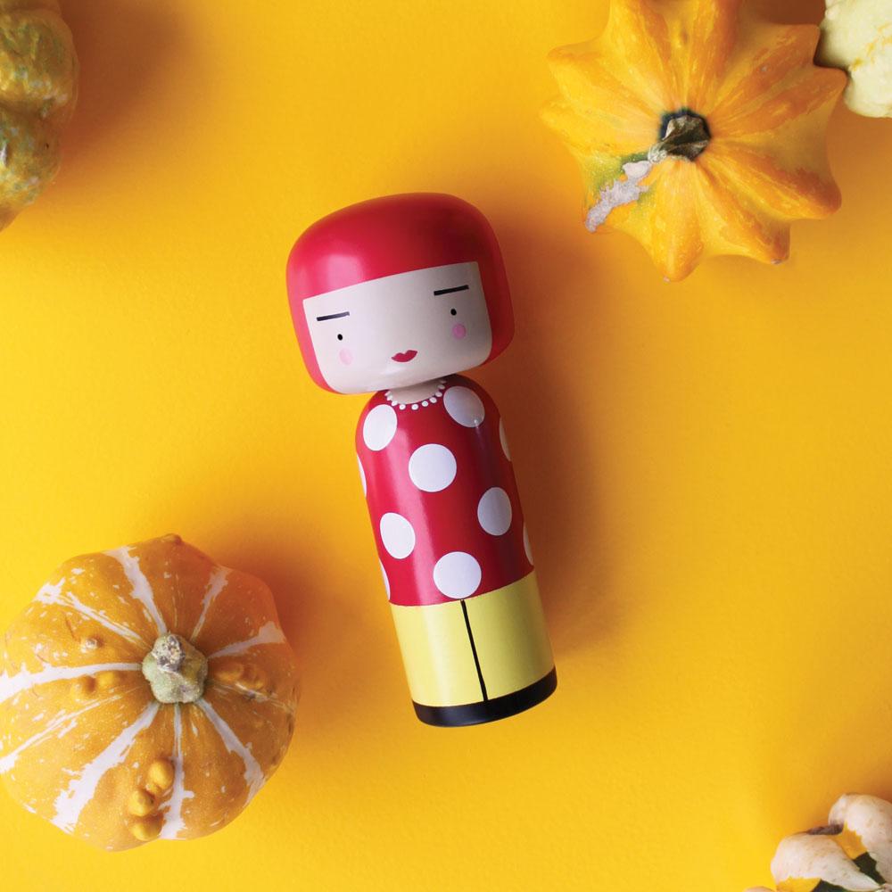 The Dot Kokeshi Doll displayed on a table with pumpkins.