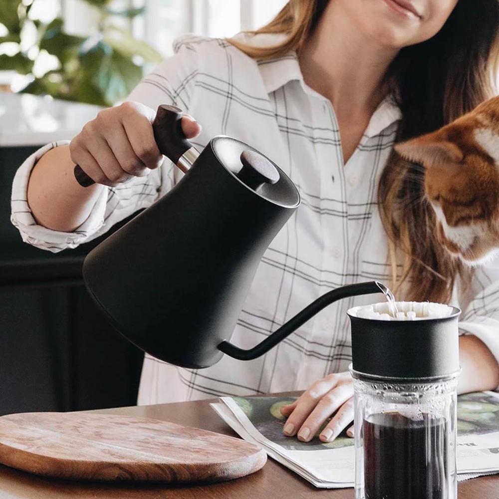 A model uses the Stagg EKG Electric Kettle: Walnut to pour water into a coffee filter.
