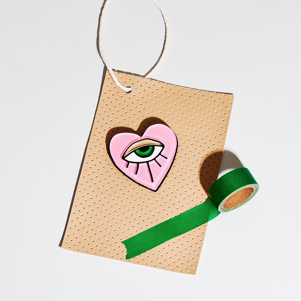 The Eye in Heart Brooch displayed on a brown label next to a small roll of green tape.