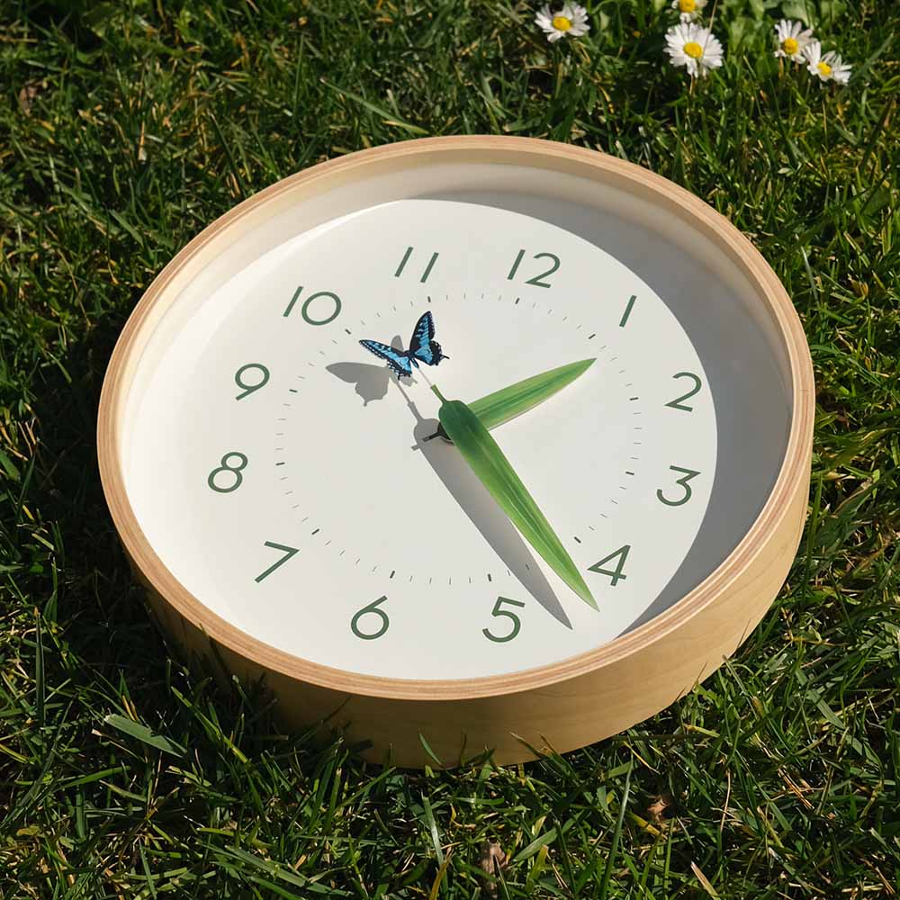 Perch Butterfly Clock resting in grass with daisies in top right corner.