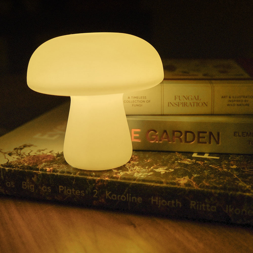 Large mushroom light, illuminated, sitting on stack of books and wood table.