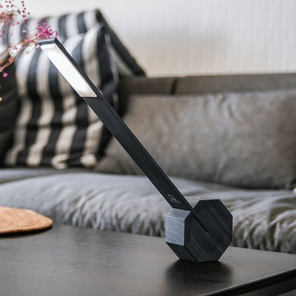 The Octagon One Desk Lamp: Black displayed on a desk in front of a couch.