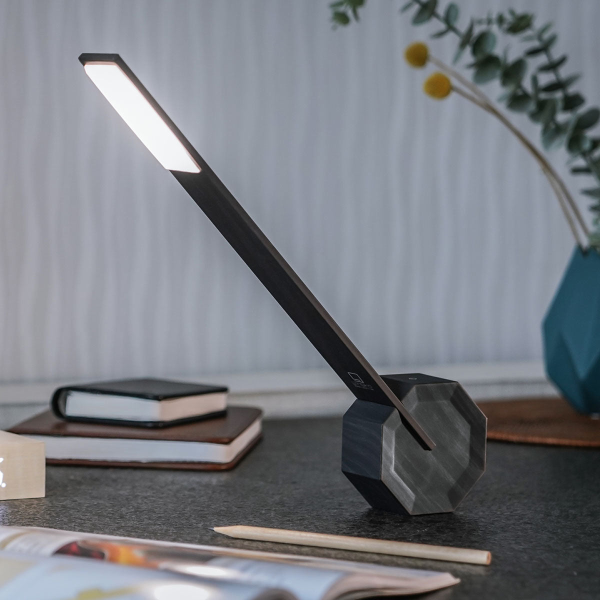 The Octagon One Desk Lamp: Black on a desk besides some books and magazines.