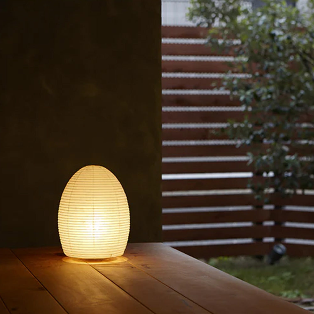 Photo of ASANO&#39;s &#39;Egg Paper Moon&#39; washi paper lamp shade illuminated on a wooden outdoor deck.