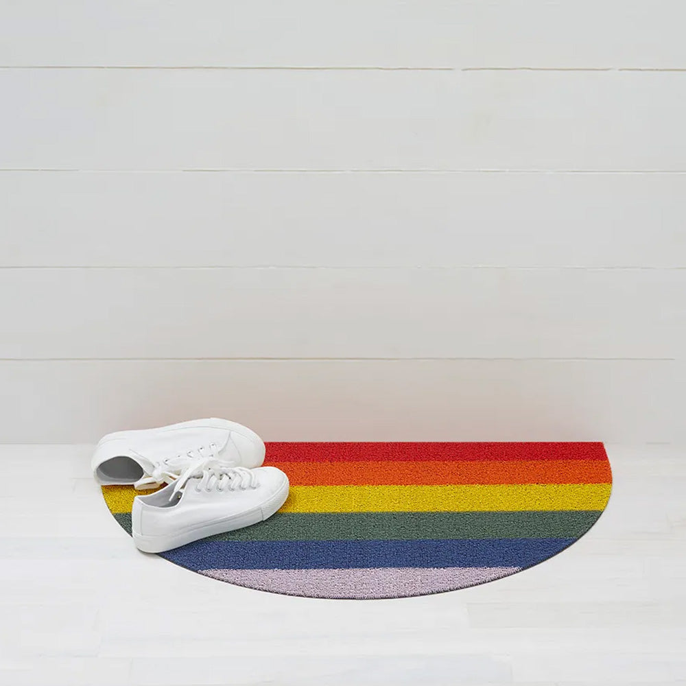 Semicircle rainbow doormat on white hardwood floors with white sneakers laying on top.
