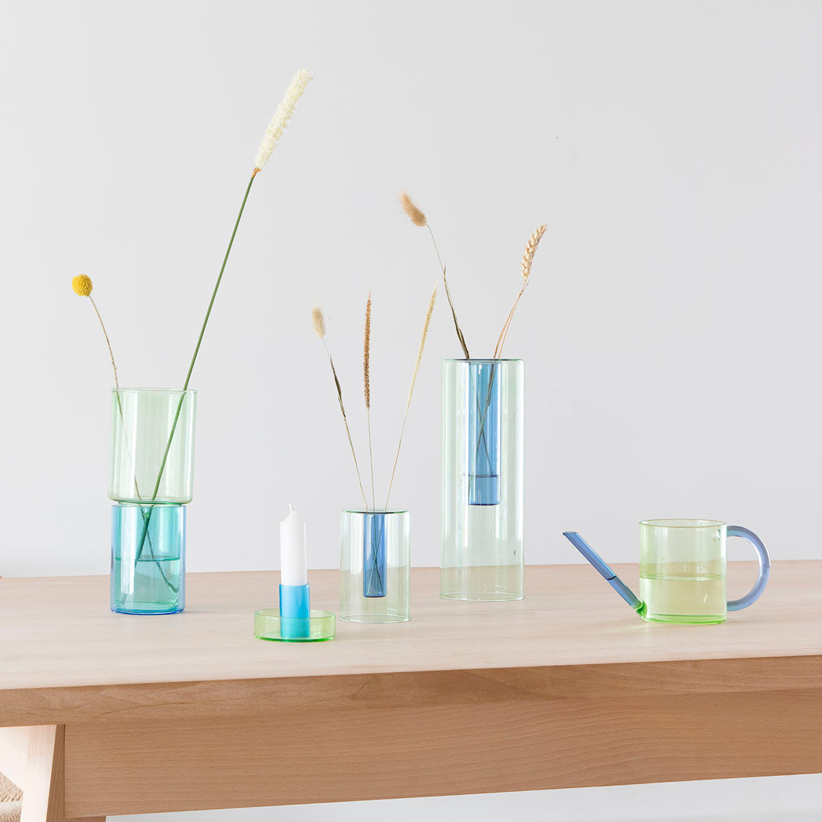 A Small Reversible Vase: Green and Blue and a Watering Can: Green and Blue displayed on a shelf with other vases.