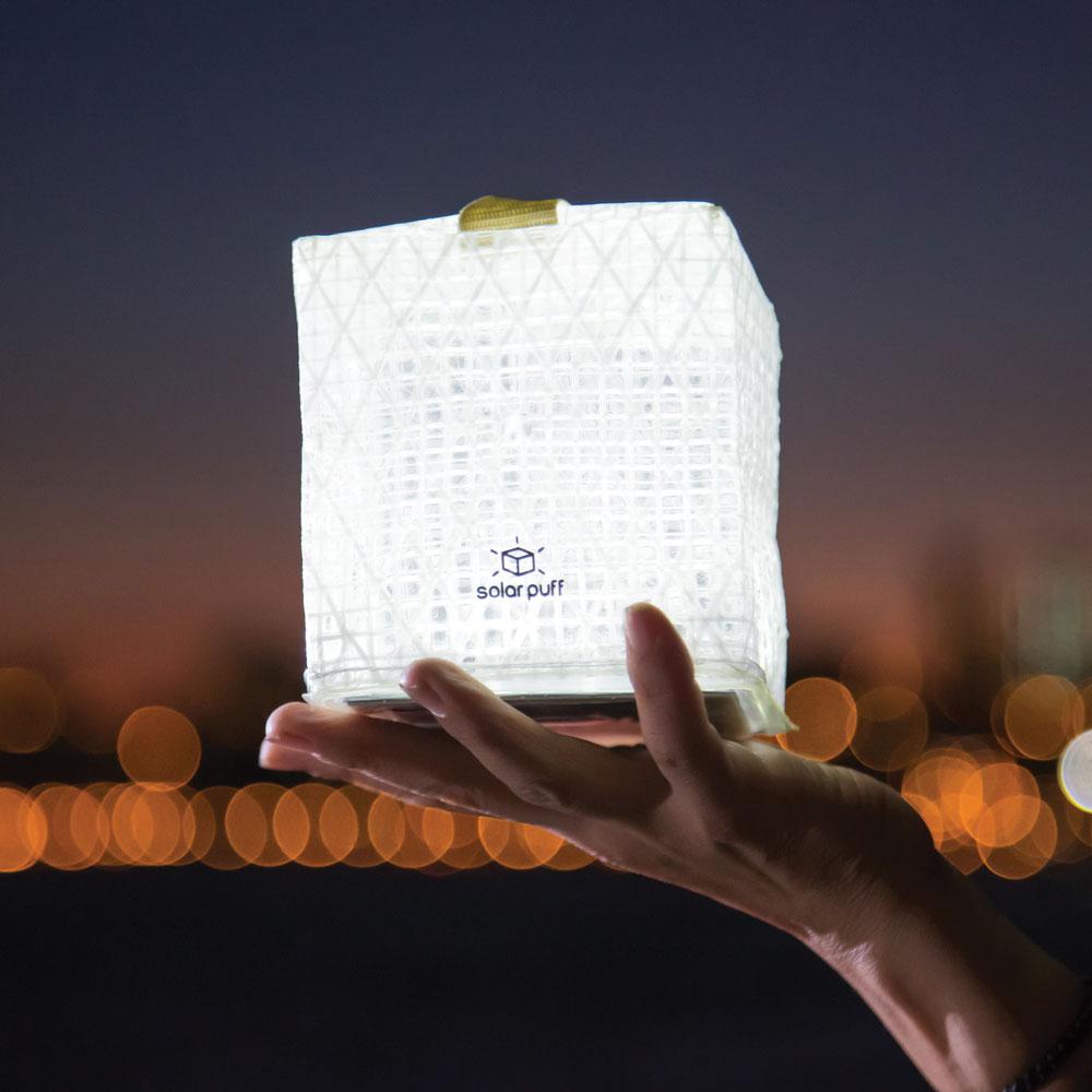 A lit SolarPuff held up by a hand at night.