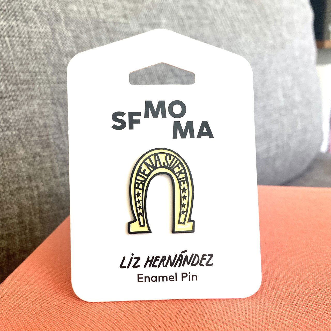 The Liz Hernández Buena Suerte Pin displayed with its packaging.